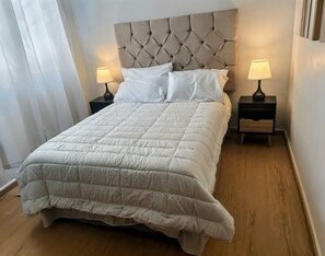 A neatly made bed with a tufted headboard, two bedside tables with lamps, and a wooden floor.