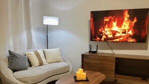 Ein Wohnzimmer mit einer Couch, einem Couchtisch mit Kerzen, einem Fernseher, der ein Feuer zeigt, und einer Lampe.