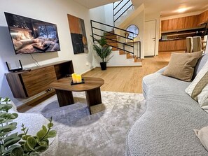 A modern living room with a sofa, a coffee table, a TV, and a staircase leading to a kitchen.