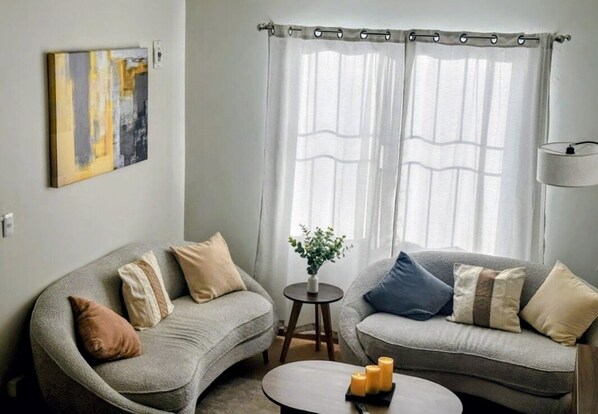 A living room with two grey sofas, a small round table with candles, and a painting on the wall.