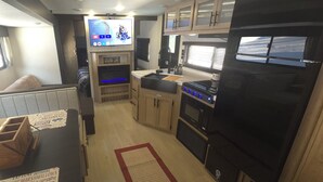 A compact RV kitchen with a TV, a stove, and a sink. - New River RV Travel Trailer with 1 King bedroom and bunks - 2 small children. (Prince)