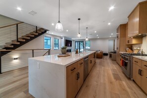 Una cocina moderna con una isla central, armarios de madera, electrodomésticos de acero inoxidable e iluminación colgante.