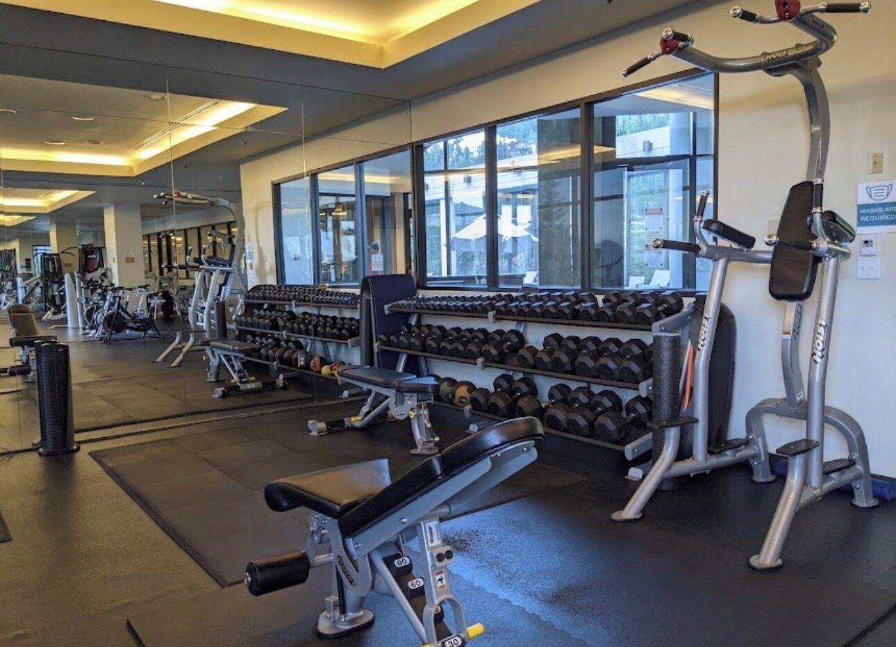 Ein Fitnessstudio mit verschiedenen Trainingsgeräten, darunter Kurzhanteln, Bänke und Kraftgeräte.
