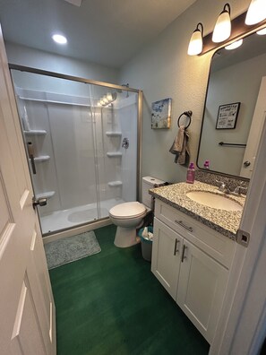 Une salle de bain dotée d’une douche à parois de verre, de toilettes, d’un lavabo avec un plan de travail en granit et d’un miroir surmonté de luminaires.