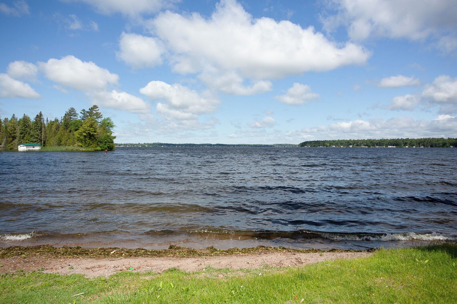 A lake with a grassy shoreline and a small building on the left.