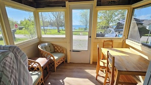 A cozy room with a wooden ceiling, a dining table, and a sofa. There are large windows offering a view of the outdoors.