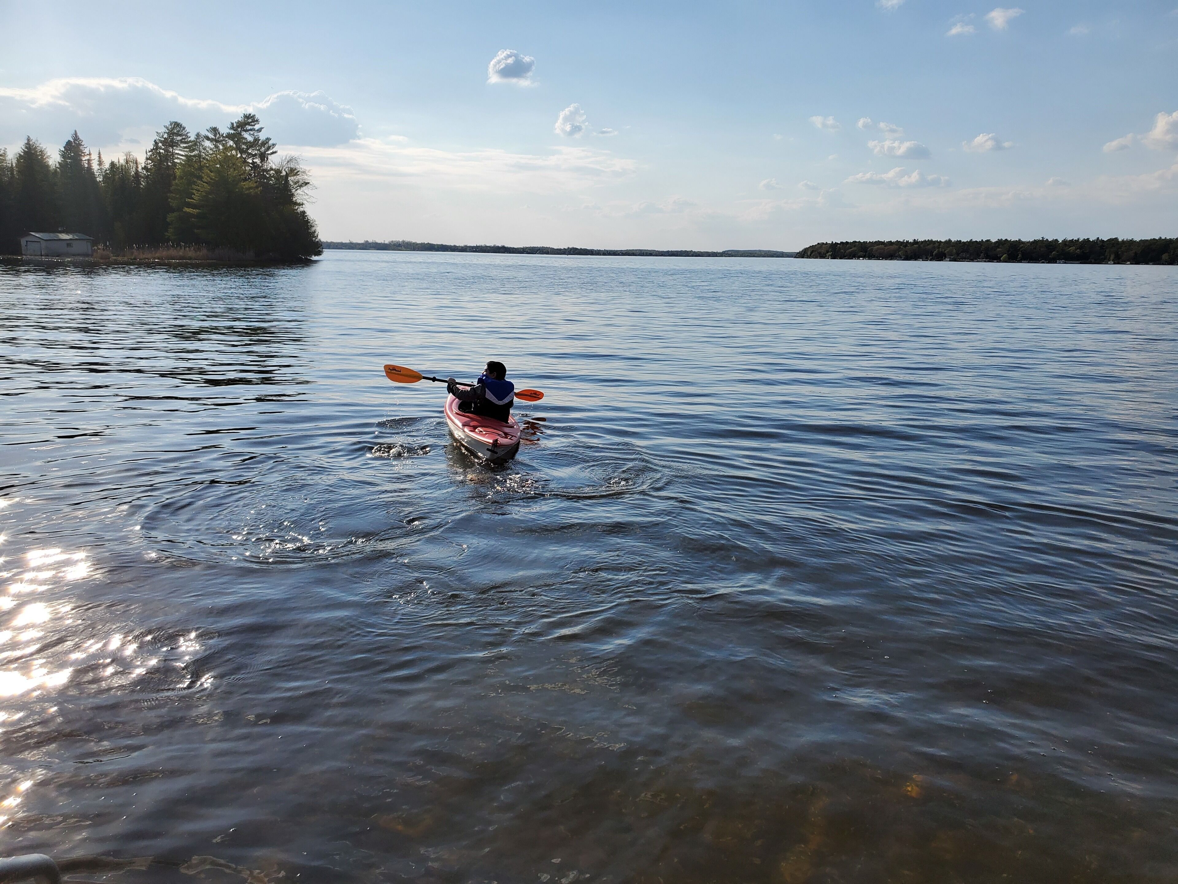 Un kayakiste sur un lac paisible, entouré d’arbres et avec une rive visible au loin.