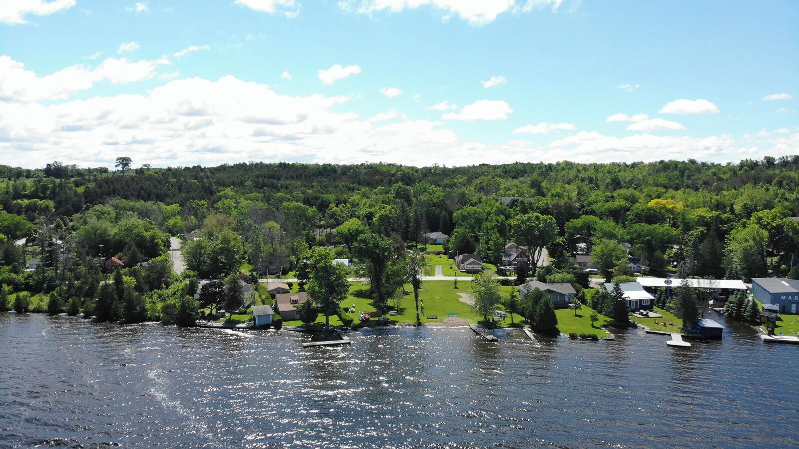 A lakeside community with houses, docks, and a forested hill in the background.