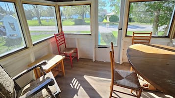 A rustic wooden room with a large table and chairs, a bench, and a window overlooking a residential area.
