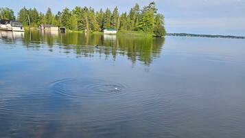 A calm lake with a boat docked on the left, surrounded by trees and a distant shoreline.