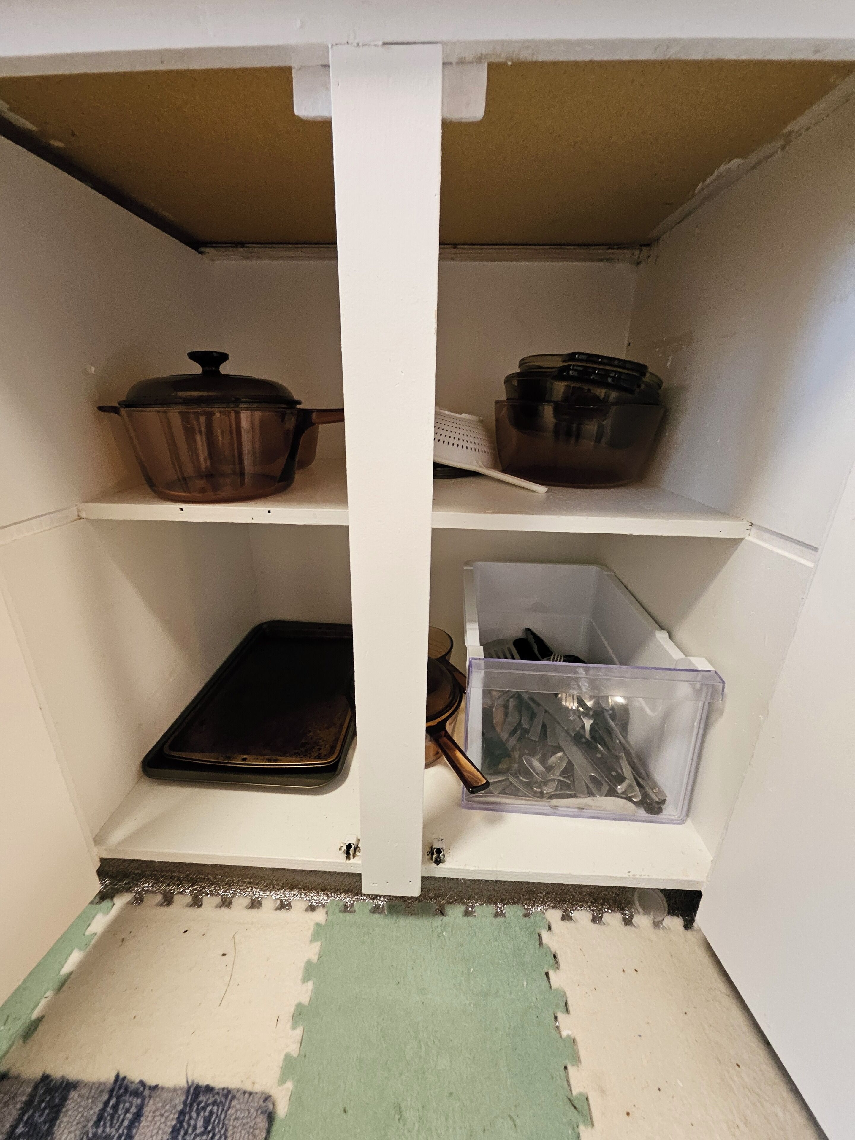 Un garde-manger de cuisine avec des étagères contenant des ustensiles de cuisine, une plaque de cuisson et un récipient en plastique.