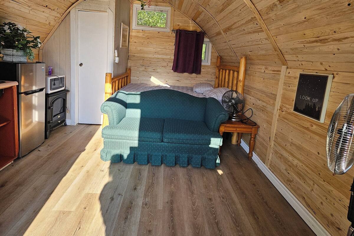 Un dormitorio acogedor en el ático, con cama, una mesita, un ventilador y una kitchenette.