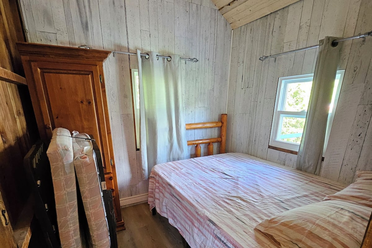 Una habitación rústica de madera con una cama, un armario de madera y una ventana con cortinas.