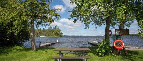 A lakeside picnic area with a bench, a lifebuoy, and a signboard.