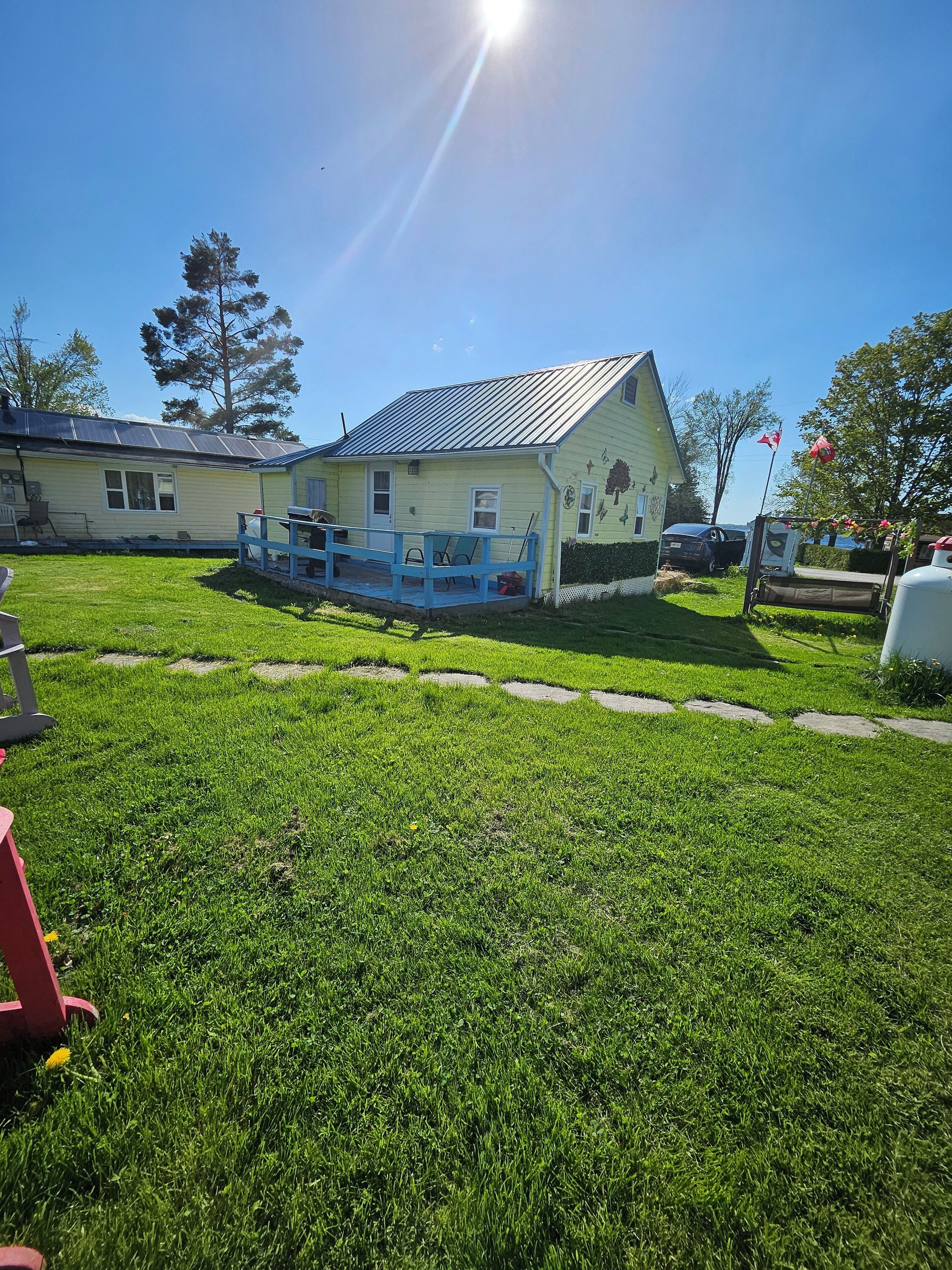 A house with a metal roof, a porch with blue railings, and a well-maintained lawn.