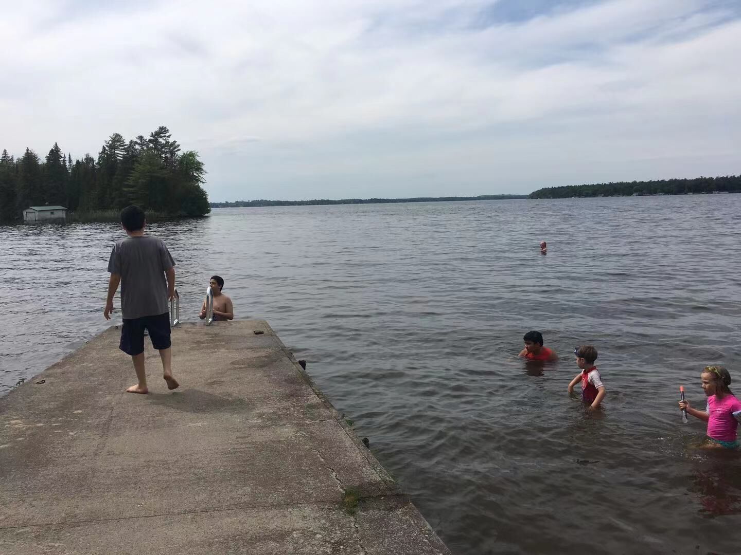 A concrete pier extending into a lake with people swimming and standing.