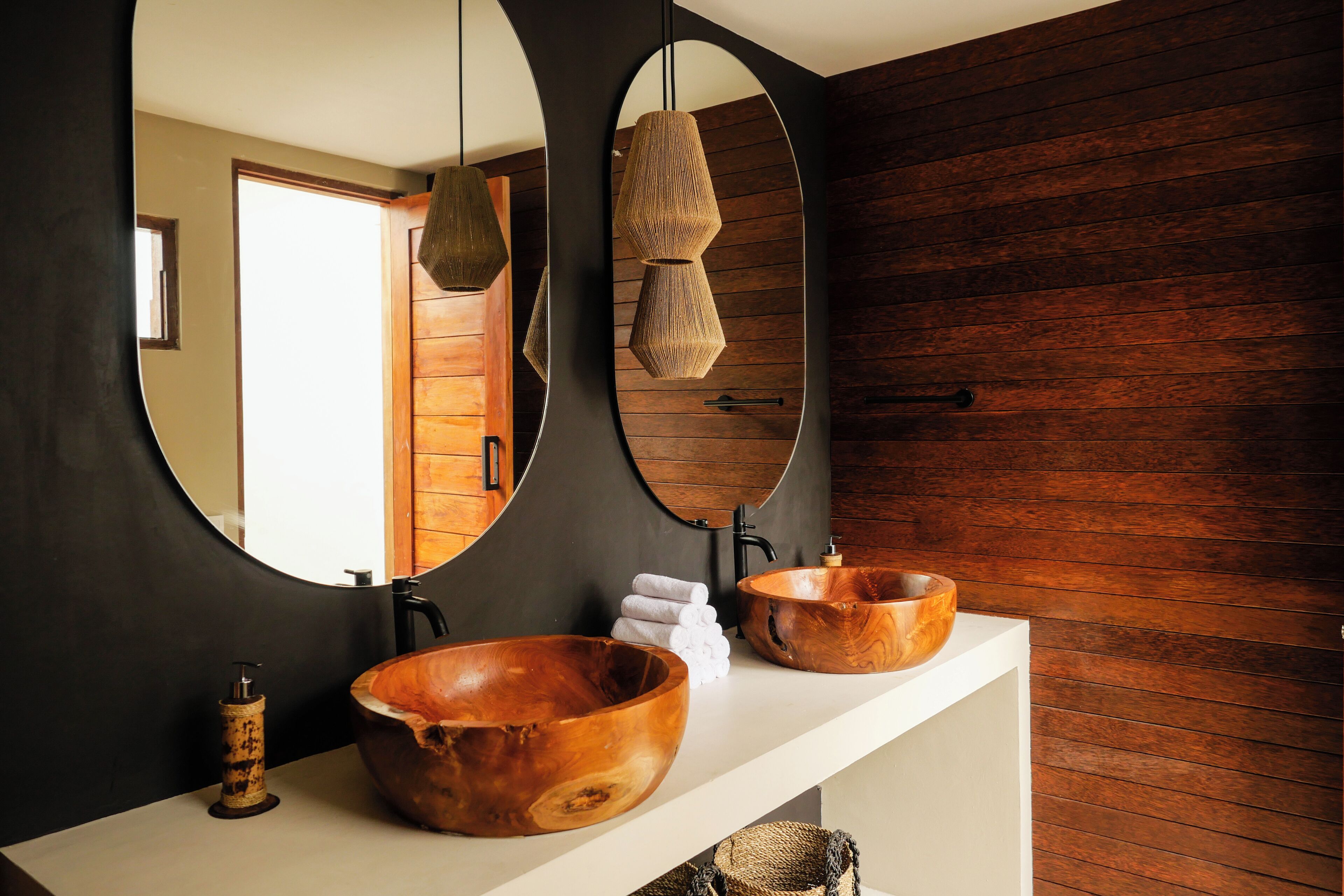 A bathroom with two wooden bowls on the counter, a mirror, and a hanging light fixture.