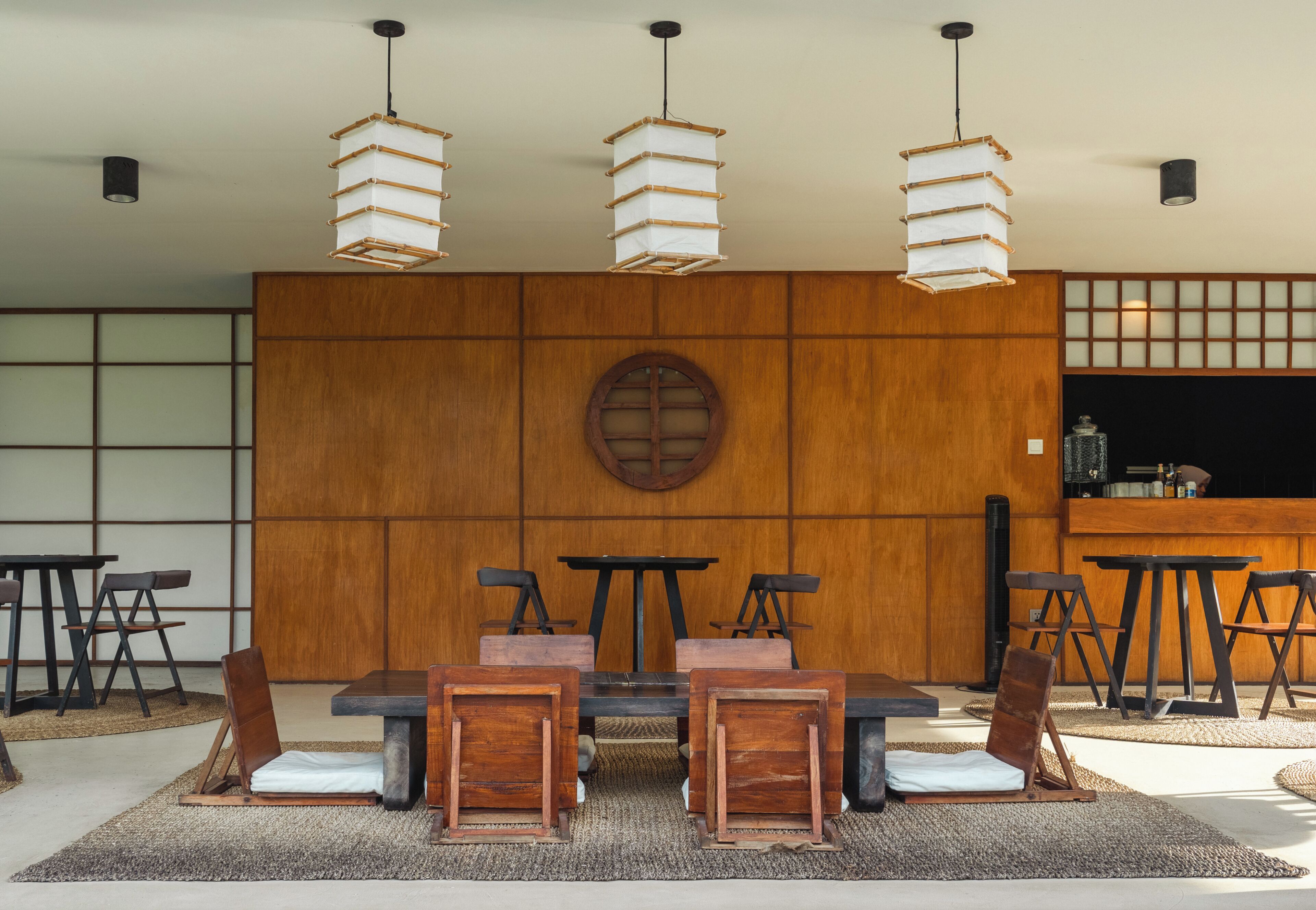 A dining area with a wooden wall, round table, chairs, and hanging light fixtures.