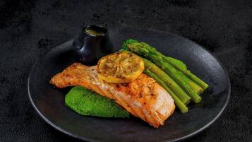 Un plato con salmón a la parrilla, espárragos y una salsa verde sobre un plato oscuro.
