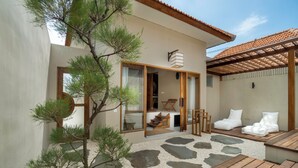 A modern outdoor patio with a wooden deck, stone pathway, and a pine tree. - YŪN Uluwatu (Pecatu)