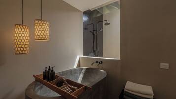 Un baño con una bañera independiente, ducha, luces colgantes y un perchero para toallas.