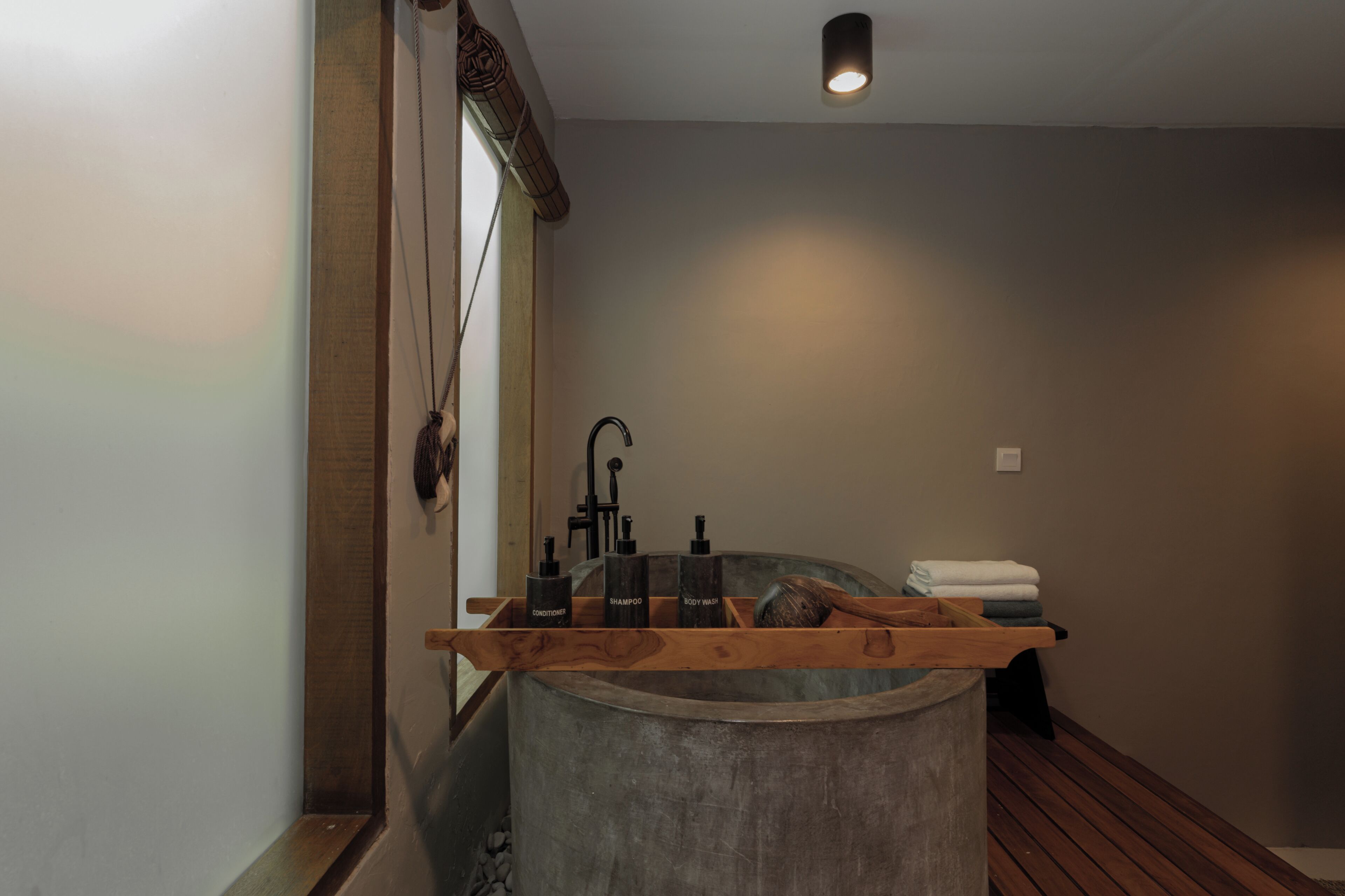 Un baño con una bañera grande, repisas de madera con artículos de aseo y un banco de madera.