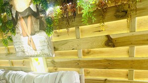 A wooden deck with a cushioned sofa and a small table with two glasses. - Studio in a green setting 15 min from the Jarry industrial zone and 2 min from the rivers. (Petit-Bourg)