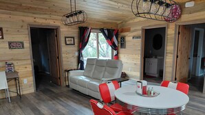 A cozy cabin interior with a sofa, a dining table with red chairs, and a kitchen area. - Relaxing 2-bedroom cabin decorated with Coke Cola Theme, (Payson)