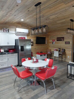 Una cocina moderna con armarios blancos, un refrigerador de acero inoxidable y un comedor con mesa redonda y sillas rojas.