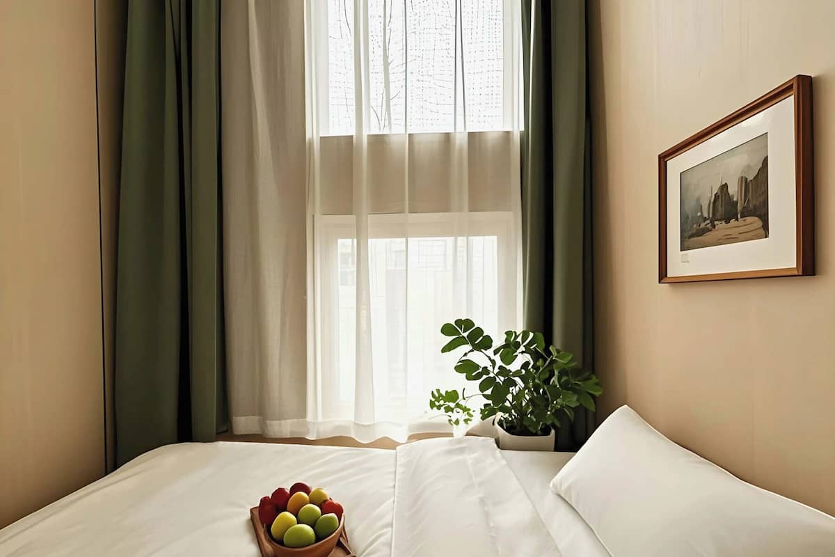 A neatly made bed with a bowl of fruit, a potted plant, and a framed picture on the wall.