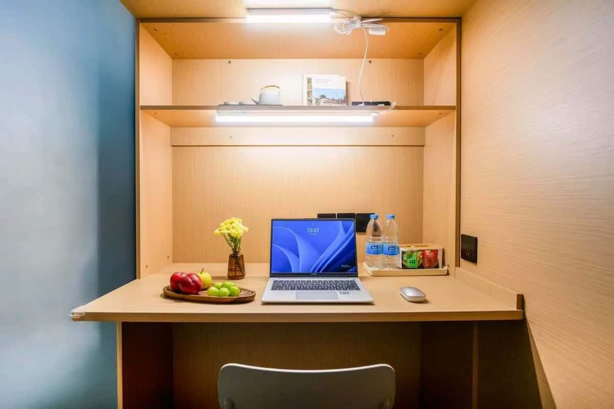 A compact workspace with a laptop, a mouse, a water bottle, and a fruit bowl.