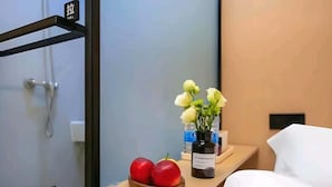 A hotel room with a bed, a wooden nightstand, a vase with white flowers, and a bottle of water. - Philosopher Hotel (Shanghai)