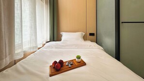 A neatly made bed with white linens, a wooden tray with fruits and a small plant, and a window with sheer curtains. - Philosopher Hotel (Shanghai)
