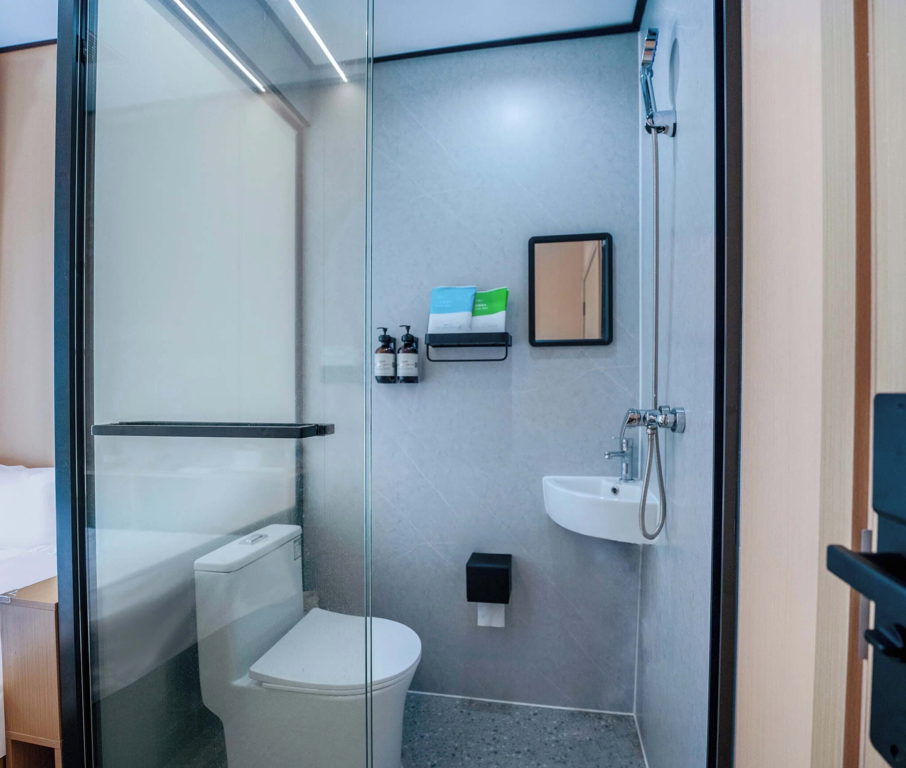 A modern bathroom with a glass partition, a white toilet, a sink, and a shower.