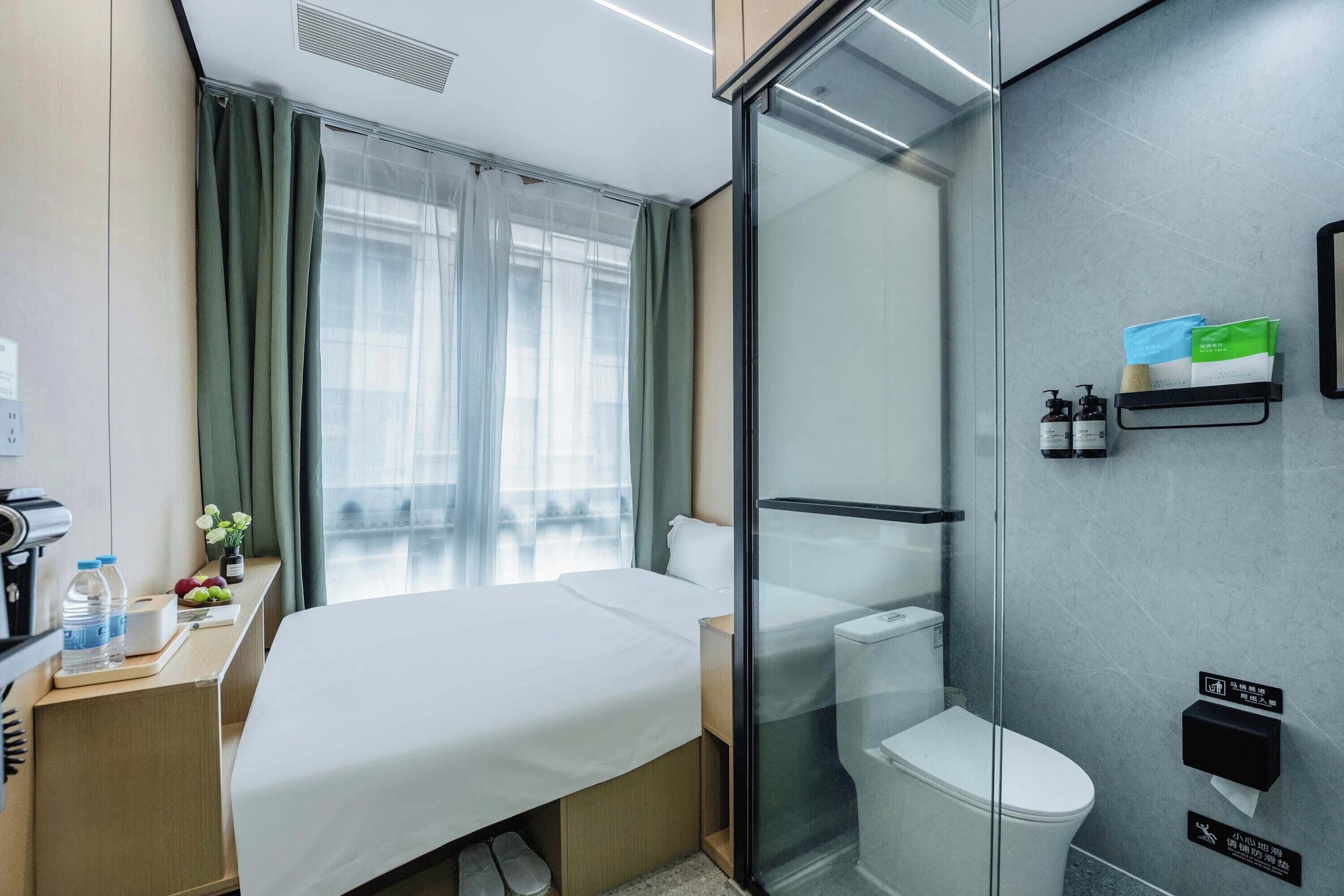 Una habitación de hotel con cama, escritorio con cafetera, ducha y retrete.