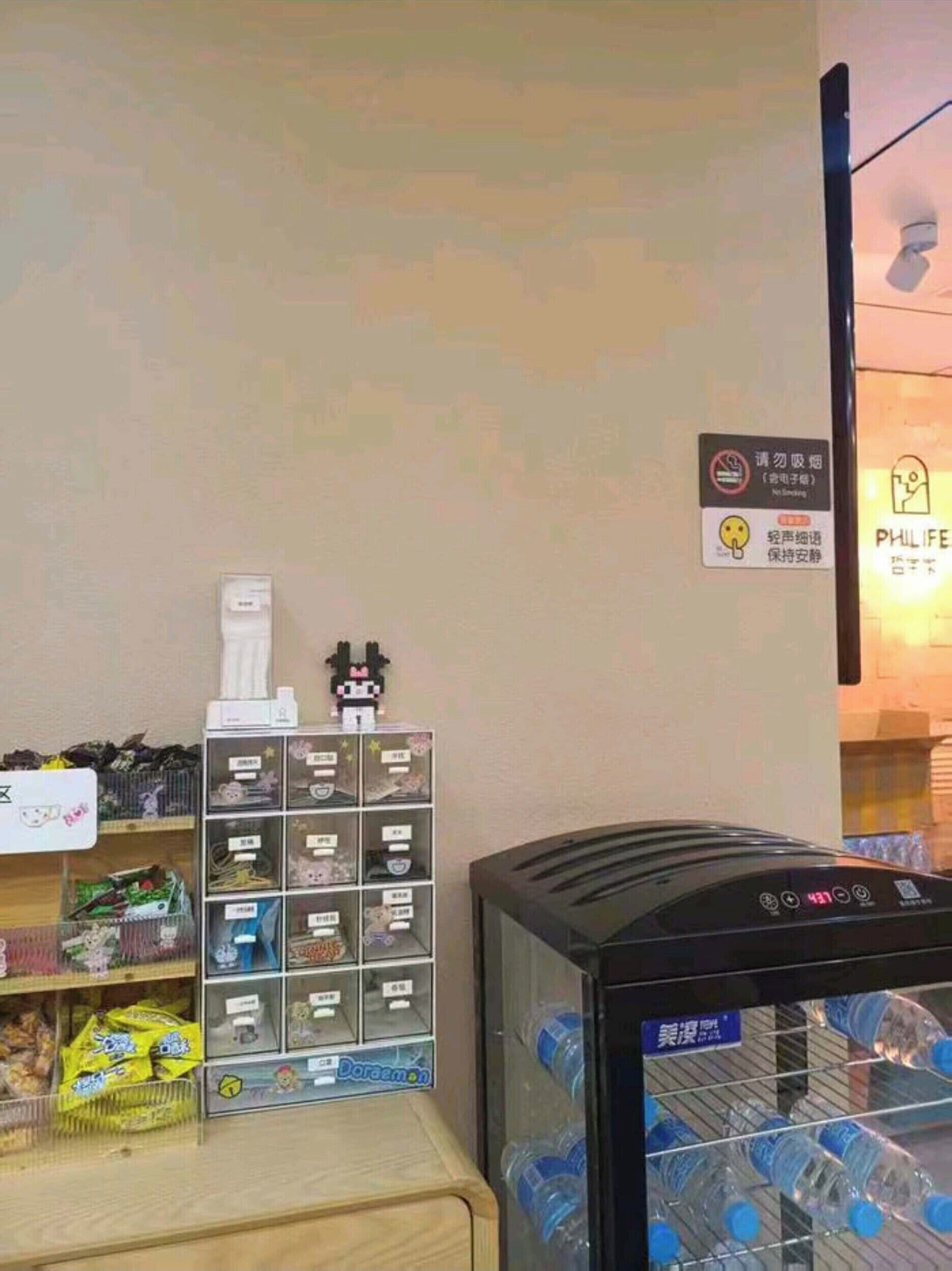 Ein Getränkeautomat mit Wasserflaschen, ein Regal mit verschiedenen Artikeln und ein Schild mit einem Rauchverbotssymbol.