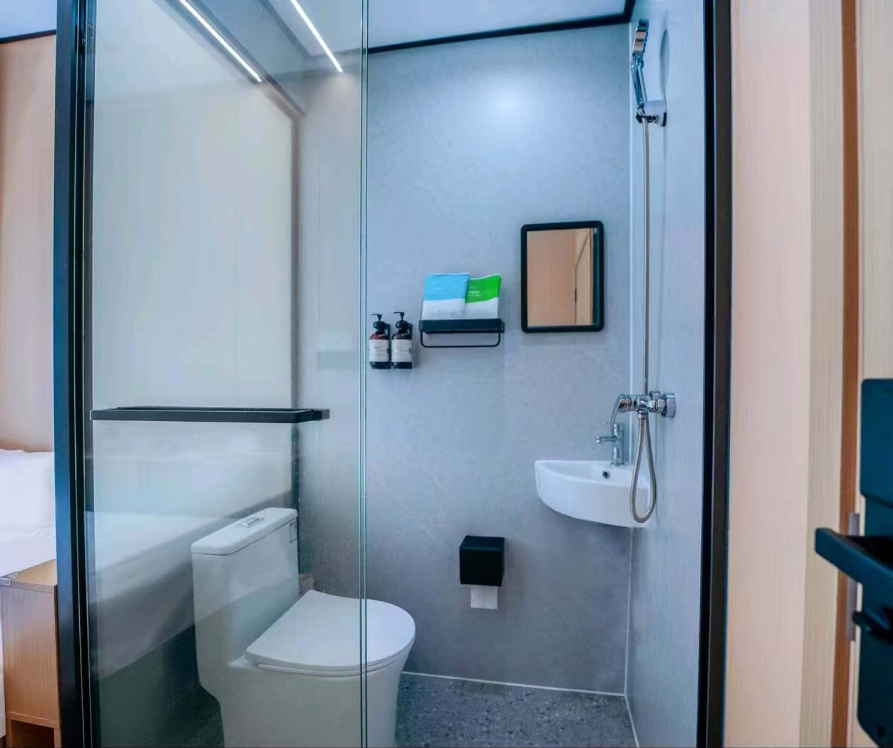 A modern bathroom with a glass partition, a toilet, a sink, and a shower.