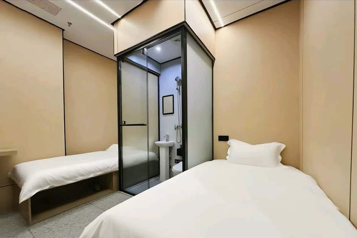A modern hotel room with a glass-enclosed shower, a single bed, and a small bedside table.