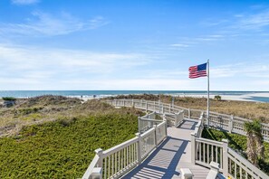 A wooden boardwalk leading to a beach with an American flag. - Oceanfront Resort Condo with Pools (Myrtle Beach)