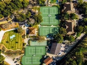 An aerial view of a residential area with three tennis courts, a swimming pool, and surrounding houses. - Oceanfront Resort Condo with Pools (Myrtle Beach)