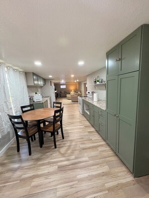 A modern kitchen with a dining area, wooden flooring, and green cabinets.