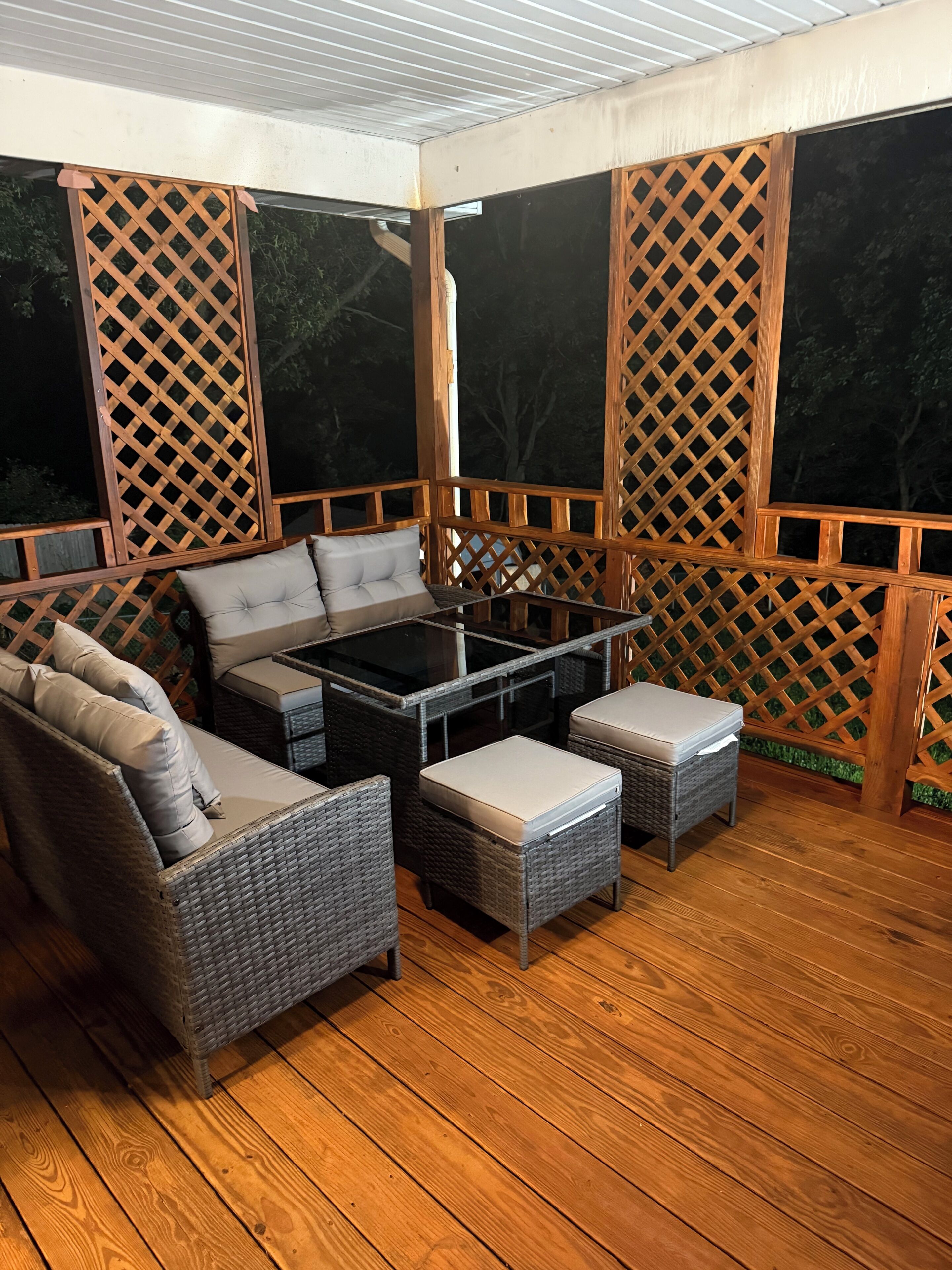 Un patio extérieur abrité, doté de meubles en osier, d’une table à plateau en verre et d’une terrasse en bois.