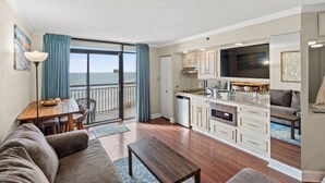 A modern apartment with a kitchen, dining area, and a balcony with a view of the ocean. - Oceanfront Condo with Lazy River (North Myrtle Beach)