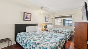 A hotel room with two beds, a wooden bench, a desk, a lamp, and a TV. - Oceanfront Condo with Lazy River (North Myrtle Beach)