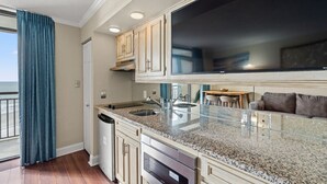 A modern kitchen with granite countertops, stainless steel appliances, and a large flat-screen TV. - Oceanfront Condo with Lazy River (North Myrtle Beach)