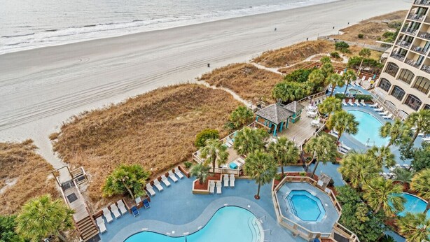 A resort with multiple swimming pools, a beach view, and a building with balconies overlooking the ocean. - Oceanfront Condo with Lazy River (North Myrtle Beach)