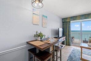Ein modernes Wohnzimmer mit Holztisch, Fernseher und einem Balkon mit Meerblick.