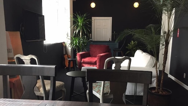 A cozy indoor seating area with a wooden table, two chairs, a red armchair, and a white sofa. There are potted plants and a television mounted on the wall. - LANAIHOTEL & DORMITORY  (Naha)