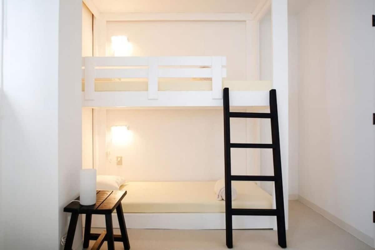 A bunk bed with a ladder, a small table, and a wall-mounted light fixture.