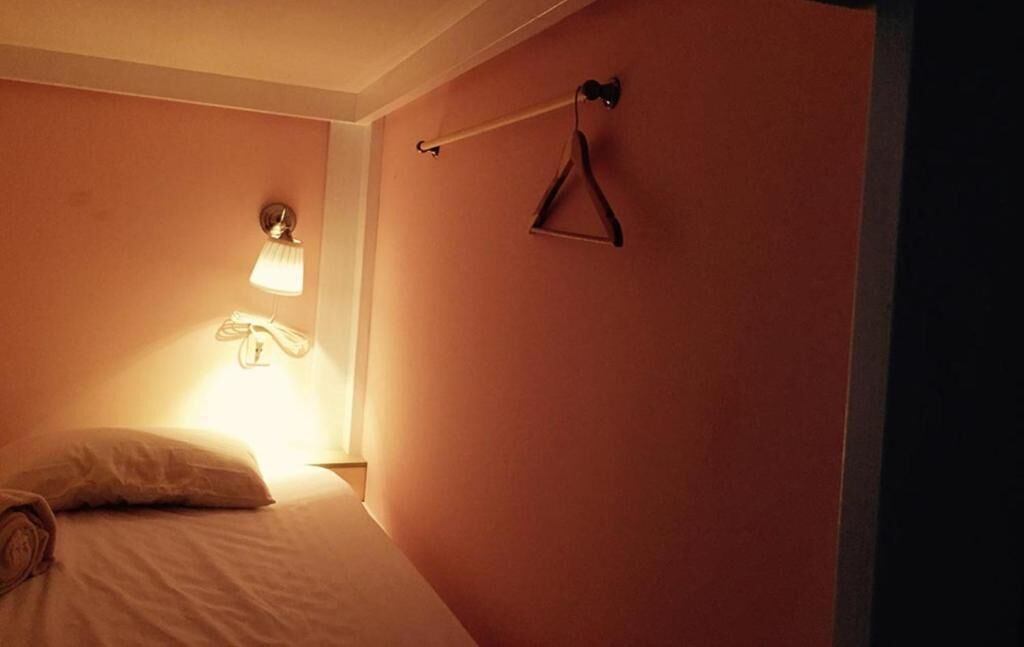 A bedroom with a bed, a hanging light, and a clothes hanger on the wall.